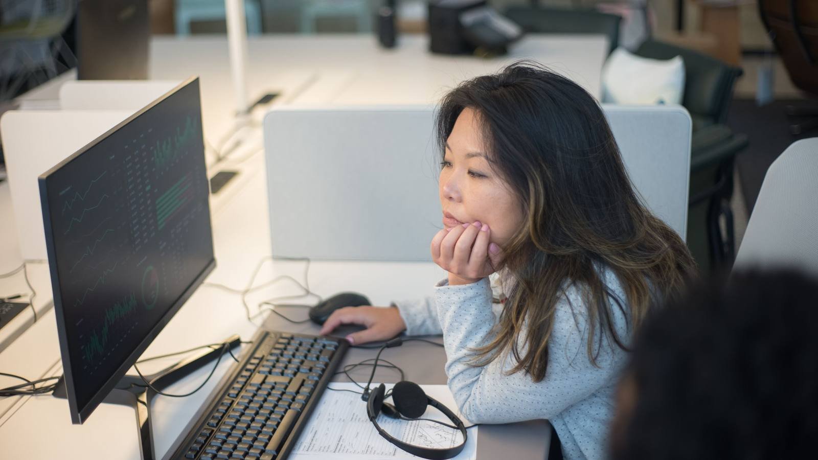 Pessoa examinando informações na tela de um computador, em um escritório
