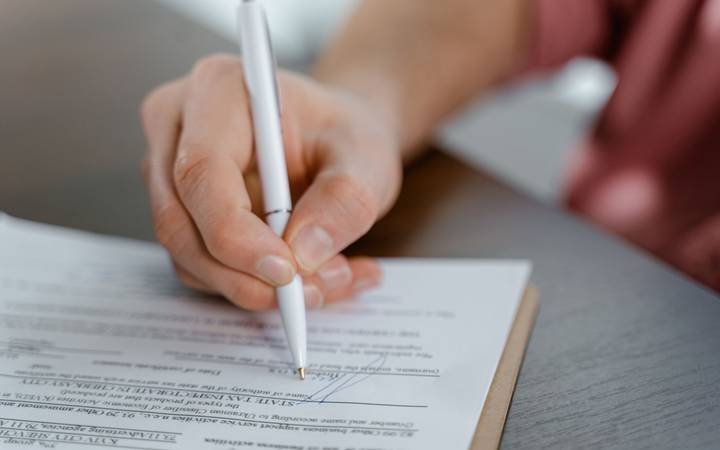 Mão assinando um documento com caneta, sobre uma mesa