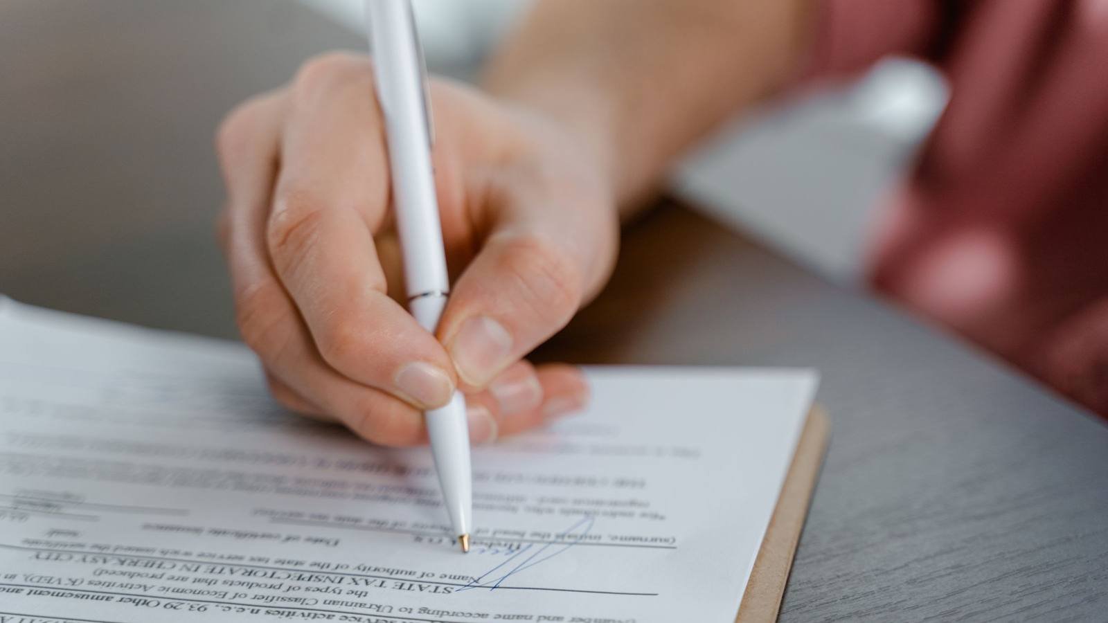 Mão assinando um documento com caneta, sobre uma mesa