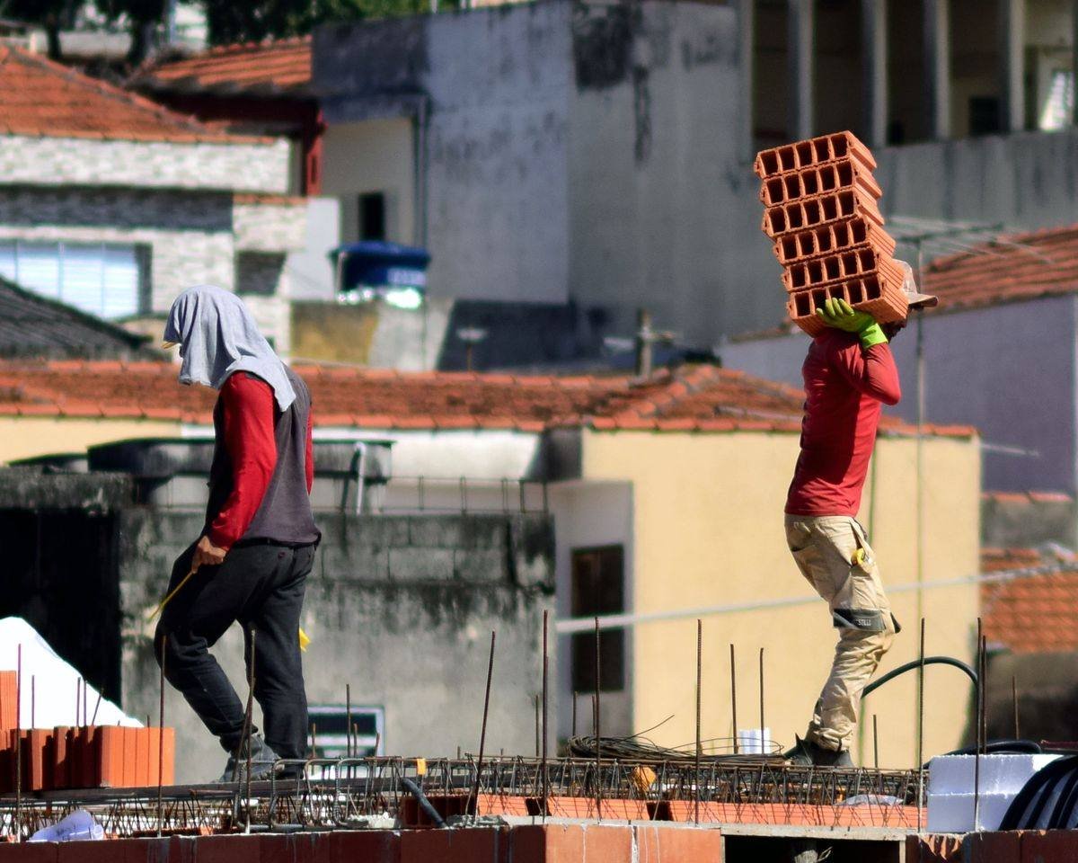 Dois pedreiros trabalhando na laje de uma construção de alvenaria, em bairro residencial brasileiro