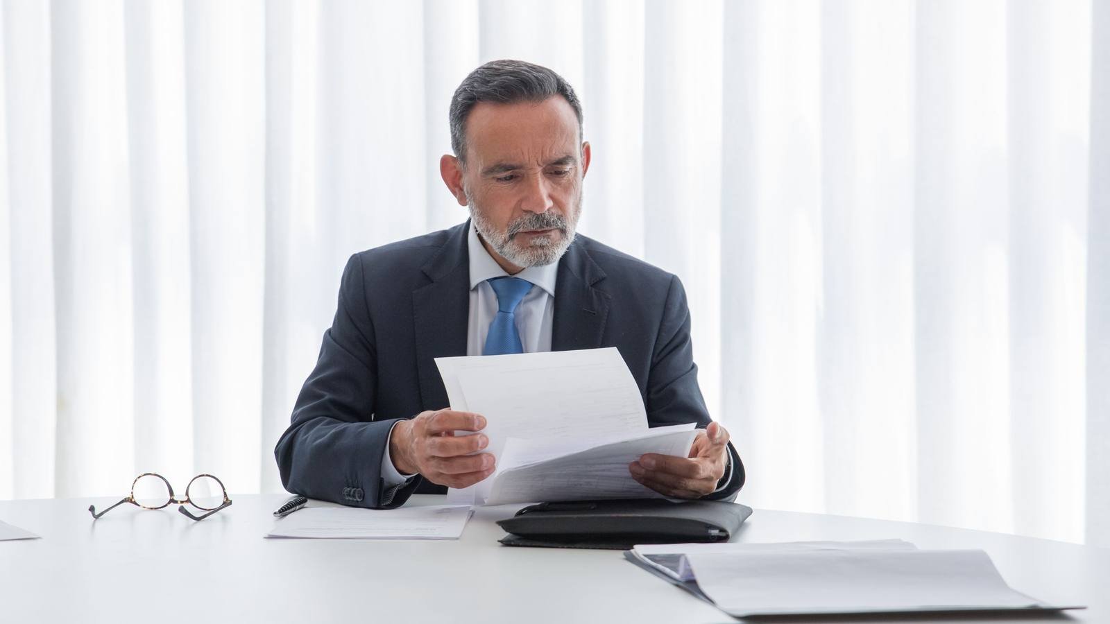 Empresário lendo um documento sentado à mesa de um escritório claro