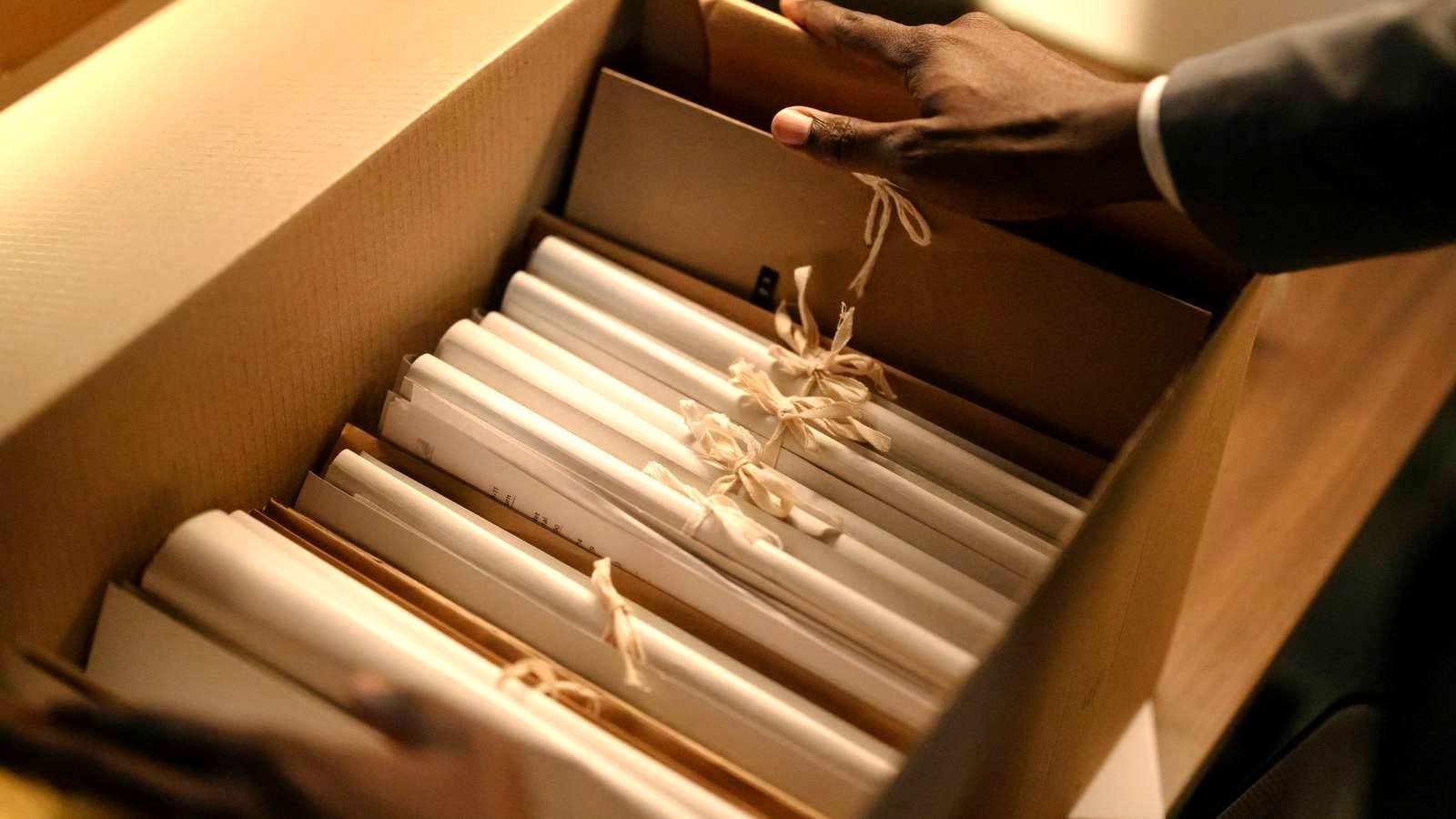 Mãos organizando pastas de documentos dentro de uma caixa de arquivo